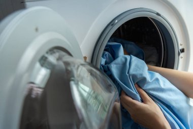 Kadının el beyaz çamaşır makinesine yükleme kirli mavi yatak örtüsü