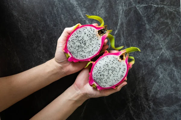 Dragon fruit in man hands with black marble background.