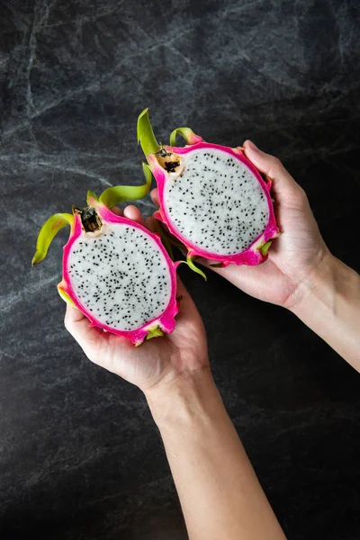 Dragon fruit in man hands with black marble background.