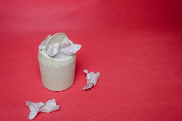 Light trash bin on red background. Closeup of crumpled sheets of paper. Concept of environmental recycling paper waste