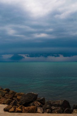 Fırtına öncesi gökyüzü deniz pürüzsüzlüğü. Ufuk çizgisi ve karanlık gök gürültülü bulutlar ile Seascape. Karanlık gökyüzüne sahip taş plajdan manzara