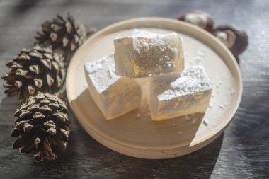 Tahta tabağa kar gibi şeker serpiştirilmiş lezzetli beyaz Türk yemeği. Çam kozalakları ve kestane fıstıklarının yanında oryantal aromalı tatlılar. Kış Noel tatlısını gün ışığında