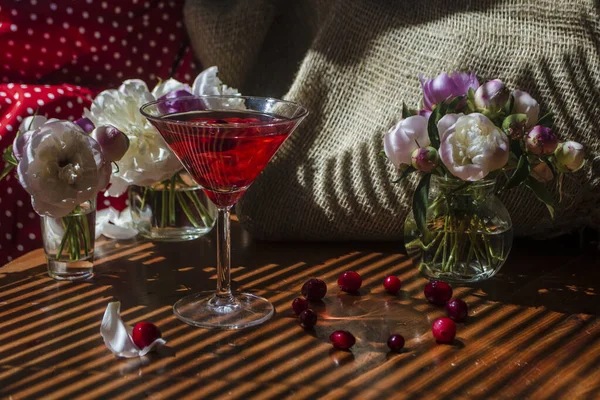 Magisches Stillleben mit einem Glas roten Getränks mit Herbstbeeren umgeben von weißen Blumen auf textilem Hintergrund im diagonal gestreiften Schatten der Jalousien an einem strahlend sonnigen Tag. Grußkarte — Stockfoto