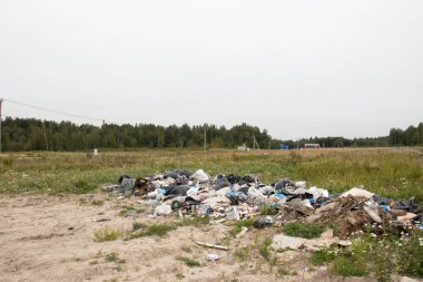 Bir tarlanın ortasında bir çöp yığını ve arka planda orman. Ekolojik sorunlar ve çevre kirliliği.