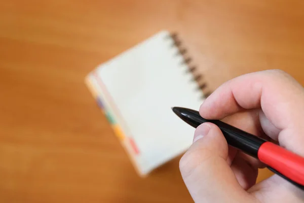 Hand holds a pen. Man makes a note in a notebook. The background is out of focus. Paper work.