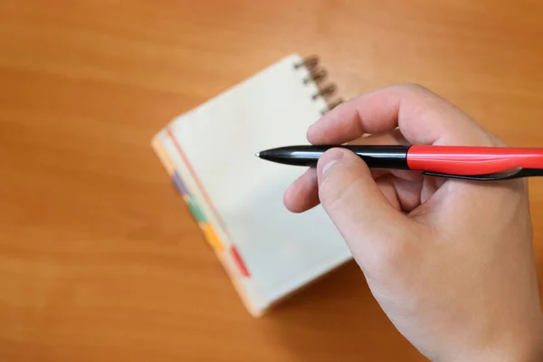 Hand holds a pen. Man makes a note in a notebook. The background is out of focus. Paper work.