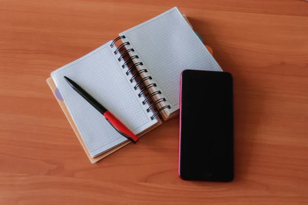 Phone with a black screen, blank notebook and pen on the table. Template for business or education. Empty space for text.