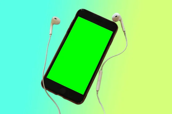 A phone with a green screen and white headphones on a color gradient background. Template for music applications or music content.