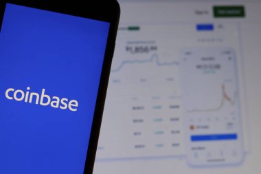 Ekranda Coinbase logosu olan cep telefonu dizüstü bilgisayardaki web sitesini kapat. Bozuk para tabanı çizelgeleriyle bulanık bir arkaplan. Los Angeles, California, Usa - 27 Ekim 2019, Illustrative Editorial
