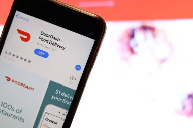 Mobile phone screen with DoorDash Food Delivery logo on app store close up with website on laptop. Blurred background. Los Angeles, California, USA - 27 October 2019, Illustrative Editorial