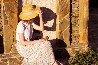 Arka planda hasır şapkalı bir kız turist. Yüzü olmayan kadın oturur. Boşluğu kadın gömleği ve eteğinin yanına kopyala.