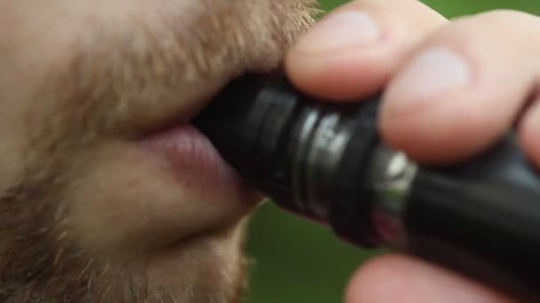 Een man inhaleert van een VAP en uitademt een dichte witte stoom in close-up op een onscherpe achtergrond. baard en snor op gezicht — Stockvideo