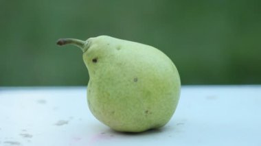 Bir çiftçinin eli açık havada yeşil bir bahçe karşı beyaz bir kırsal masada olgun bir yeşil armut alır. hasat mevsimi.