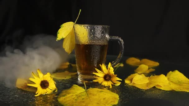 秋の風景の真っ只中に熱いお茶のスタンドの雨から濡れた透明なガラスのマグカップに来ています 黄色の落ち葉 黄色の花 秋の気分 — ストック動画