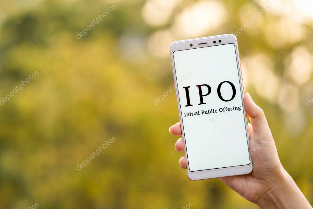 Initial Public Offering concept. Young female hand holding mobile phone & showing IPO which is displayed on it's screen in outdoor background with copy space. LIC IPO.