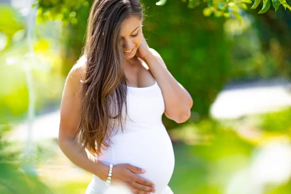 Usmívající se těhotná žena stojící venkovní držení rukou na břiše — Stock fotografie
