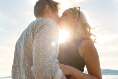 Sahilde güneşin altında öpüşen romantik bir çift.