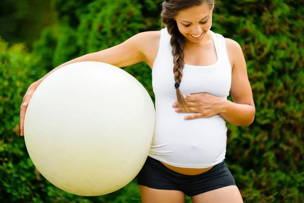 Těhotná žena dotýká břicho při držení Fitness míče v parku — Stock fotografie