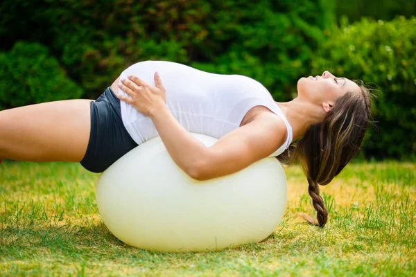 Embarazada hembra con los ojos cerrados estirándose de nuevo en la bola de yoga — Foto de Stock