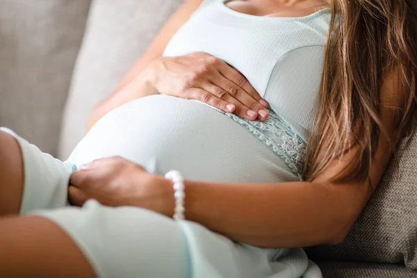 Hamile kadın kanepe elleri göbek, oturan Close-up — Stok fotoğraf