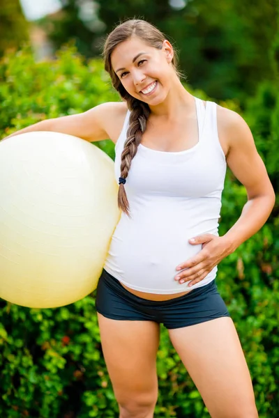 Happy těhotná žena dotýká břicho při držení Fitness míče — Stock fotografie
