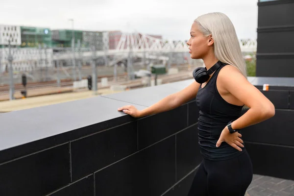 Ajuste atleta femenina con auriculares y Smartwatch descansa después del entrenamiento en el puente —  Fotos de Stock