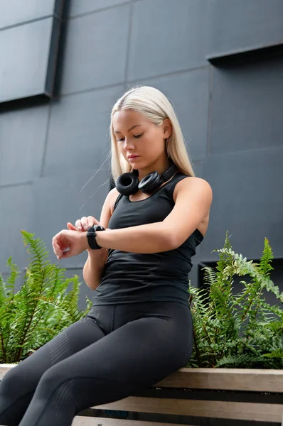 Mujer comprueba el rendimiento del entrenamiento en el reloj inteligente en la ciudad —  Fotos de Stock
