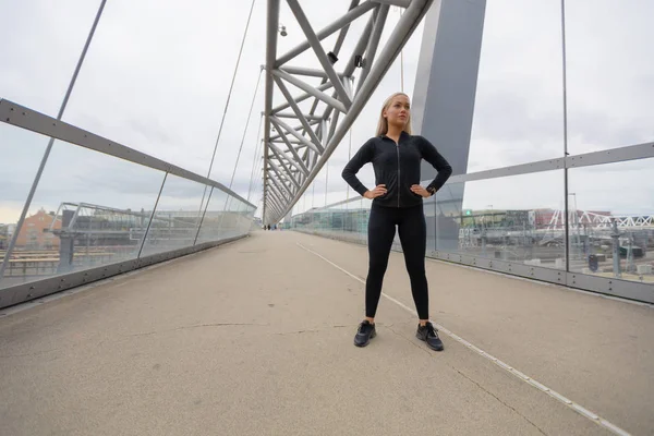 Mujer segura con las manos en la cadera en traje de entrenamiento de pie en el puente — Foto de Stock