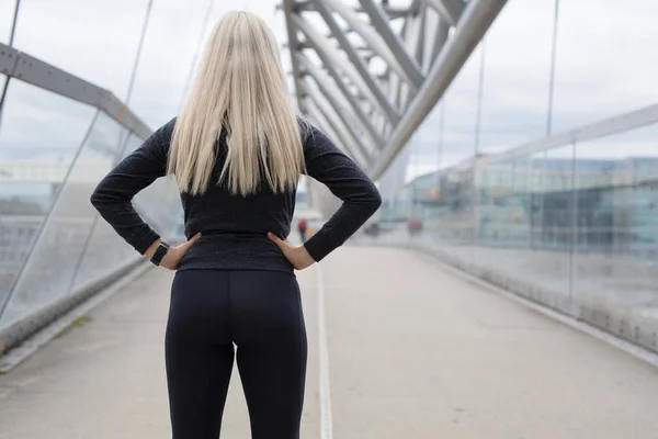 Fitte blonde Läuferin steht auf Brücke in modern aussehender Stadt — Stockfoto