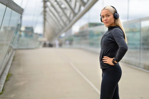 Mujer sonriente con traje de entrenamiento negro Escucha música en los auriculares —  Fotos de Stock