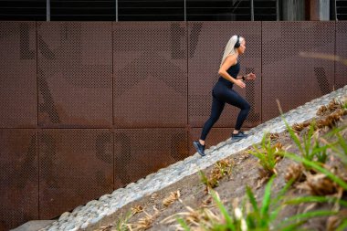 Fit sports women running interval workout in stairs against a metal wall in city clipart