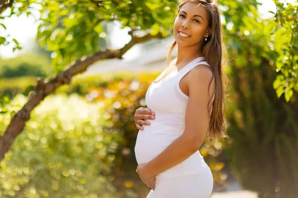 Femme enceinte souriante debout dans le jardin tenant la main sur le ventre — Photo