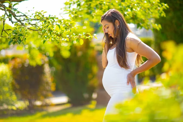 Femme enceinte dans un beau jardin regardant son ventre — Photo