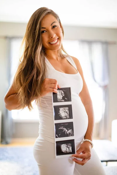Счастливая беременная женщина держит ультразвуковые фотографии на животе — стоковое фото