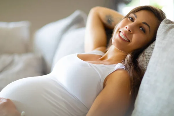 Красивая беременная женщина лежит на диване с рукой на животе — стоковое фото