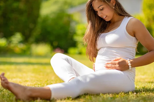 Thoughtful pregnant woman sitting on the grass in her garden — Stock Photo, Image