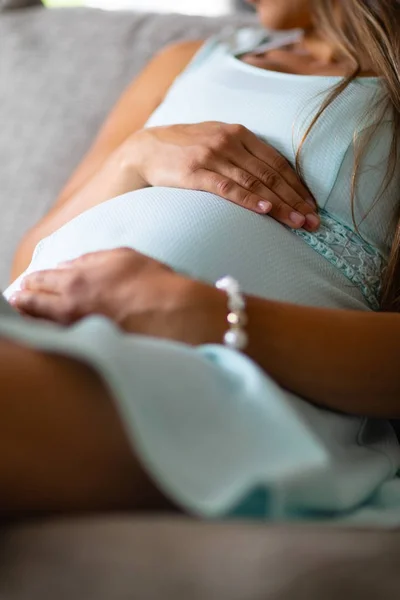 Средняя часть беременной женщины, сидящей на диване с руками на животе — стоковое фото