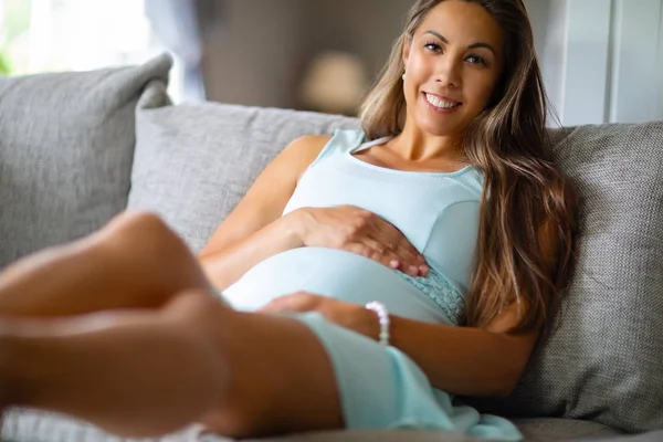 Позитивна вагітна жінка в сукні лежить на дивані будинку — стокове фото