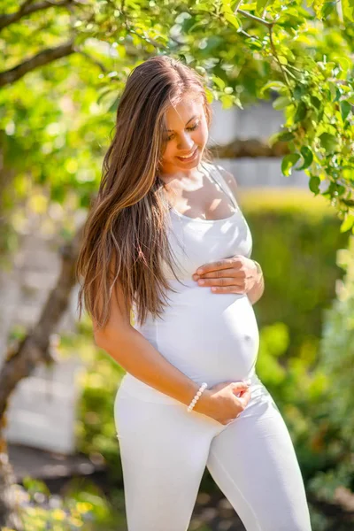 Щаслива вагітна жінка під деревом дивиться вниз на живіт — стокове фото