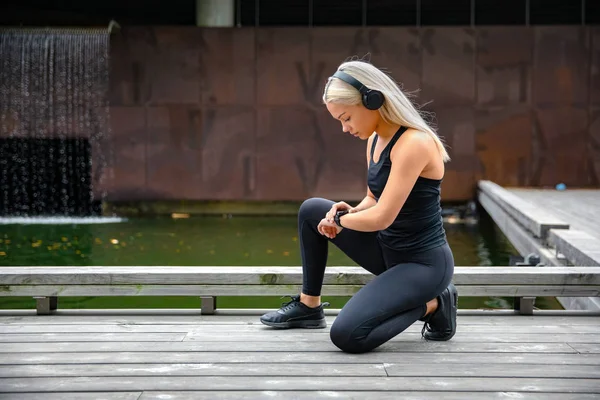 Corredor femenino deportivo escuchando música en los auriculares y usando Smartwatch —  Fotos de Stock