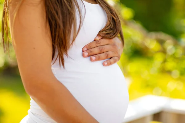 Средняя часть беременной женщины стоит на открытом воздухе, держа руки на животе — стоковое фото