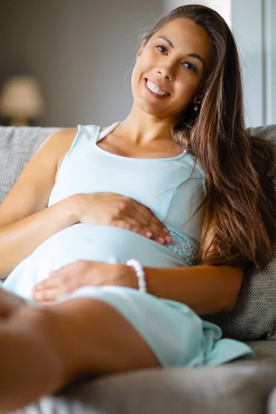 Положительная беременная женщина в платье на диване, держась за живот — стоковое фото