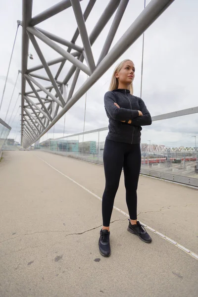 Mujer confiada en el desgaste de entrenamiento negro de pie en el puente moderno en la ciudad —  Fotos de Stock