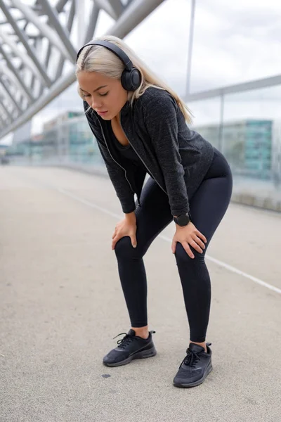 Mujer cansada descansando con las manos en las rodillas después de correr el entrenamiento —  Fotos de Stock