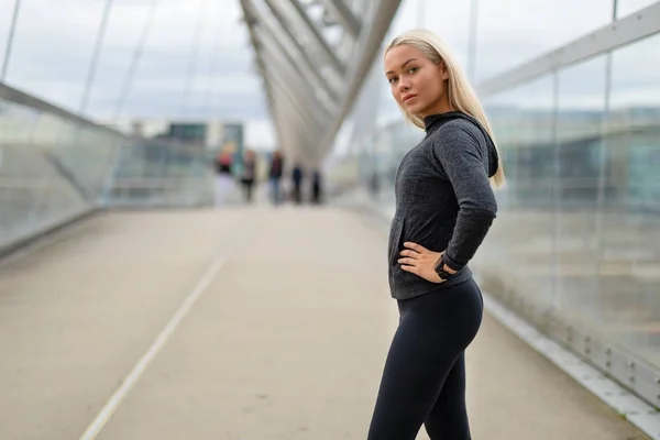 Deportiva mujer en traje de entrenamiento negro de pie en el puente moderno en la ciudad —  Fotos de Stock