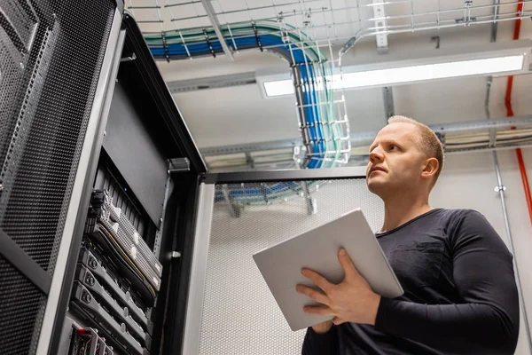 Erwachsener männlicher Techniker hält digitales Tablet in der Hand und analysiert Server im Rechenzentrum — Stockfoto