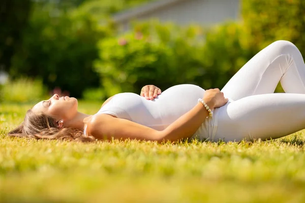 草の上に横たわる白い服を着た美しい妊婦 — ストック写真