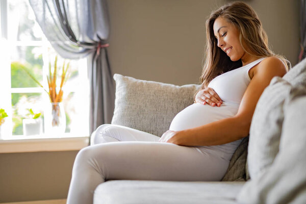 Smiling pregnant woman sitting in sofa looking at her stomach