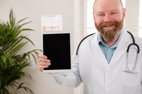 Улыбающийся взрослый мужчина-врач показывает цифровое изображение или отчет на планшете — стоковое фото
