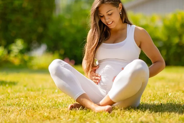 Terhes nő fehér ülve Grass szabadban Holding has — Stock Fotó